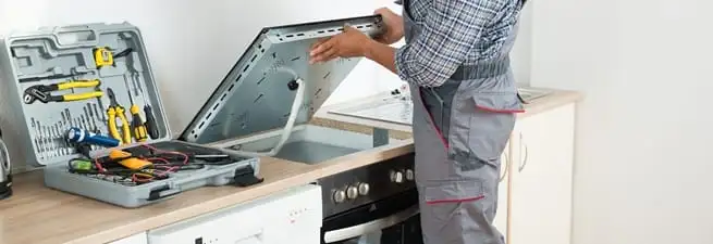 Cooktop repair technician lifting a built-in stovetop for service in Albuquerque, NM