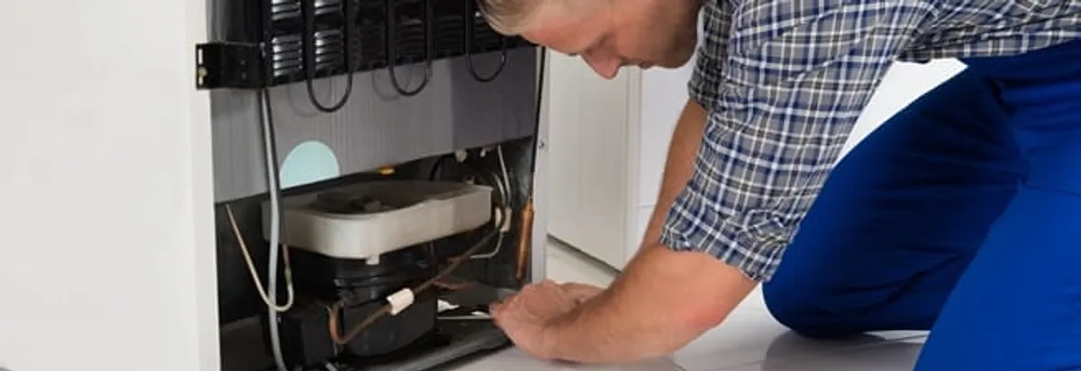 Refrigerator repair technician servicing the compressor and condenser area in Albuquerque, NM